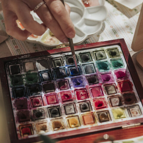 Mano de artista seleccionando color de una paleta profesional de acuarelas durante sesión de live painting en evento corporativo