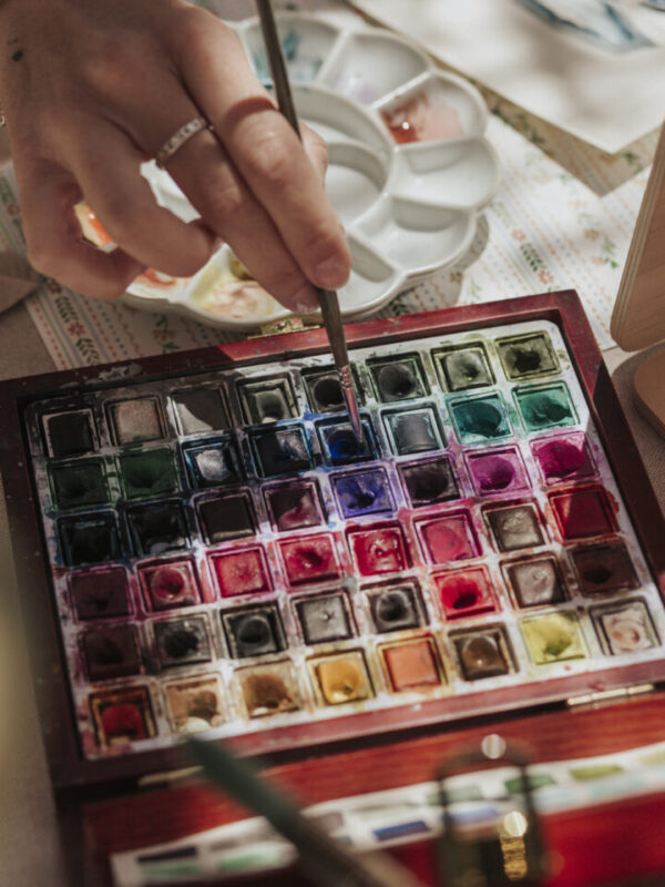 Mano de artista seleccionando color de una paleta profesional de acuarelas durante sesión de live painting en evento corporativo