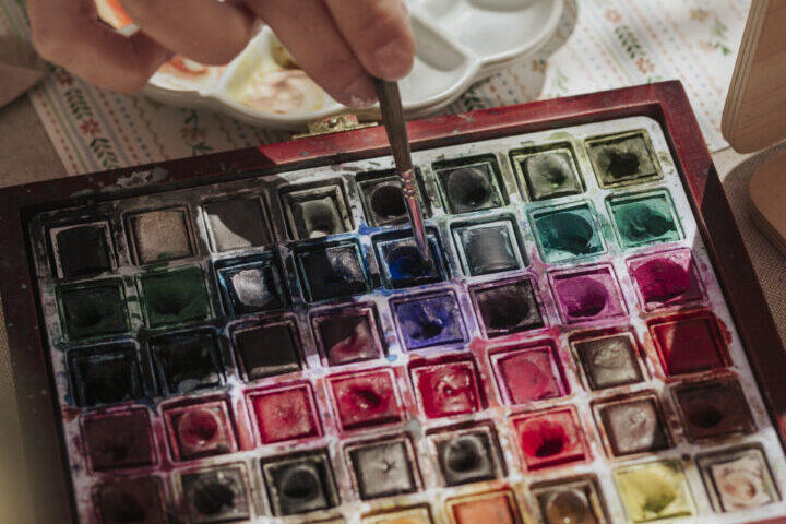 Mano de artista seleccionando color de una paleta profesional de acuarelas durante sesión de live painting en evento corporativo