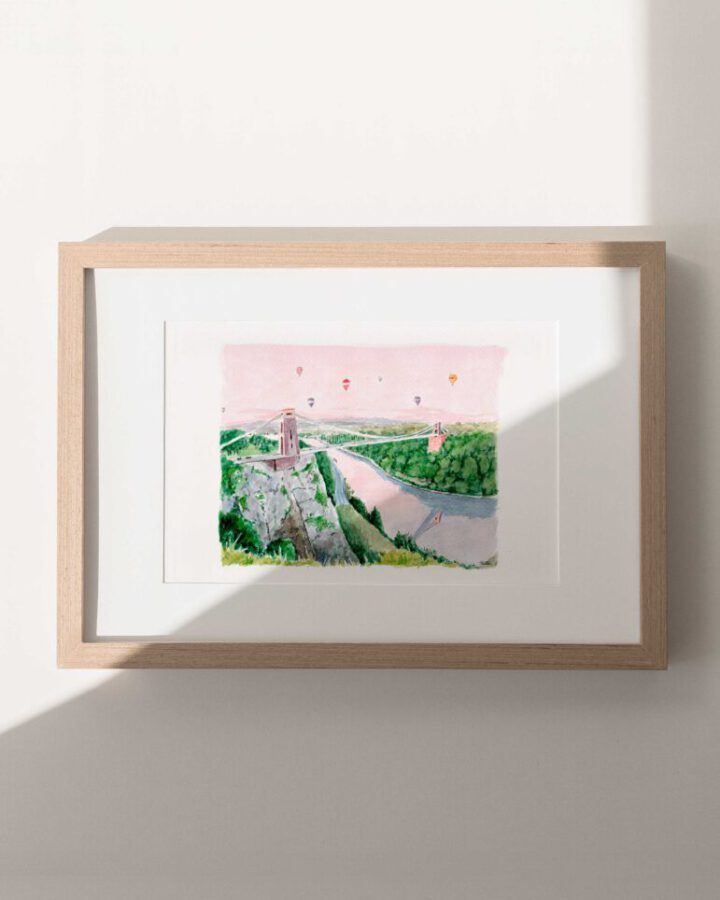 Lámina ilustrada de la ciudad de Bristol pintada en acuarela a mano con el puente colgante de Clifton y globos aerostáticos en cielo rosado