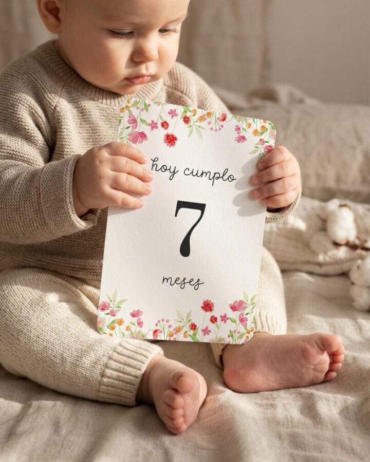 Bebé sujetando una tarjeta cumplemés con ilustración floral y número 7