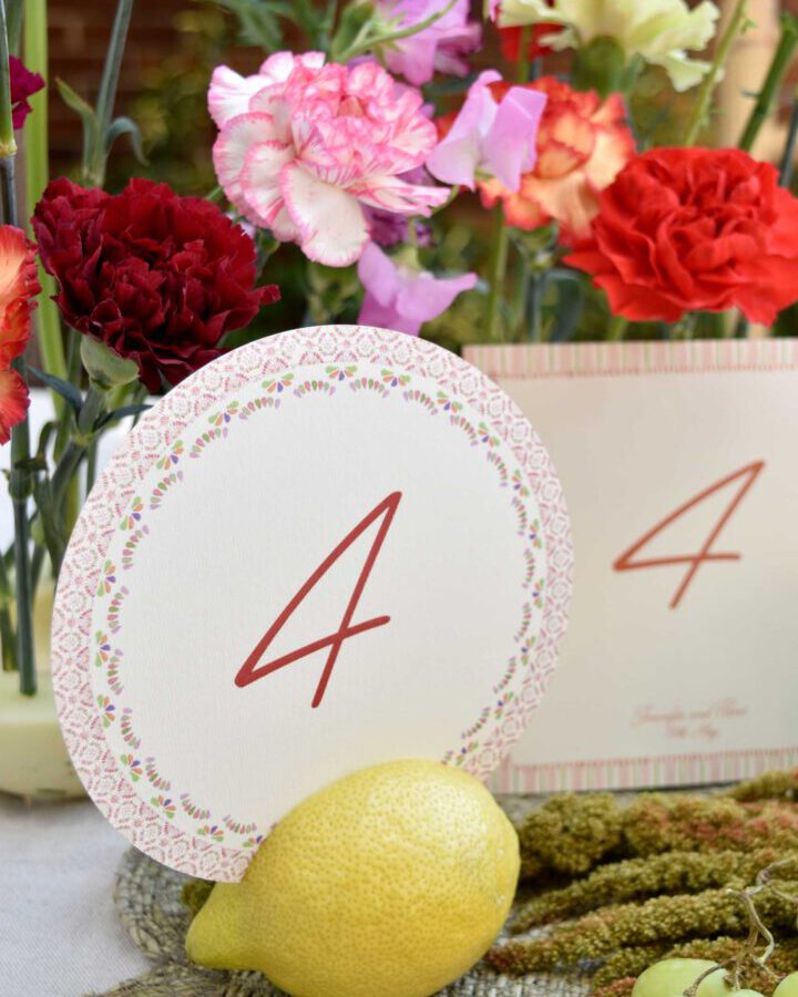 Mesero circular de boda con número cuatro en caligrafía elegante y borde decorativo con patrón de azulejos en tonos terracota