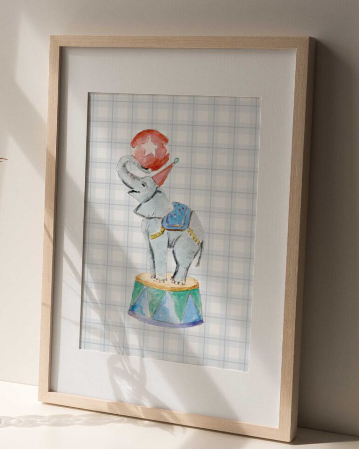 Cuadro enmarcado con ilustración artesanal de elefante de circo pintado en acuarela con chaleco azul y pelota roja sobre pedestal