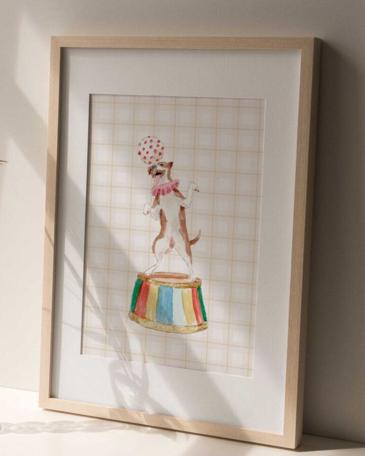 Lámina enmarcada con ilustración de perro de circo pintado en acuarela con tutú rosa equilibrando una pelota sobre pedestal colorido