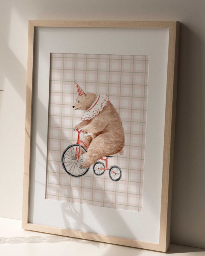 Lámina enmarcada en madera natural con ilustración en acuarela de oso de circo montando en triciclo sobre fondo de cuadrícula suave