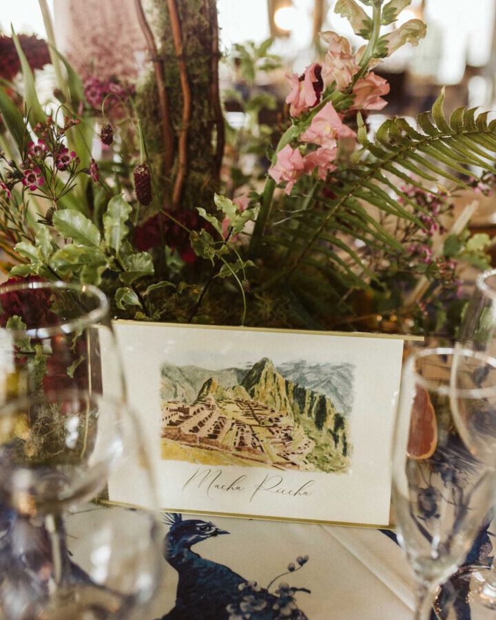 Invitación de boda personalizada con ilustración artesanal en acuarela de Machu Picchu sobre mesa decorada con vegetación natural