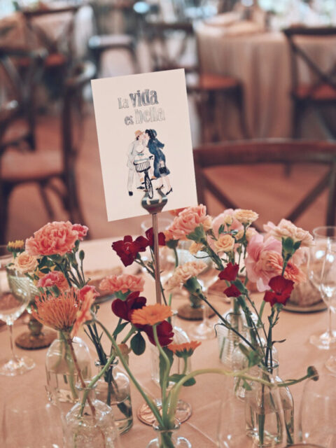 Mesero de boda personalizado con ilustración en acuarela de La vida es bella sobre mesa nupcial decorada con flores y detalles elegantes
