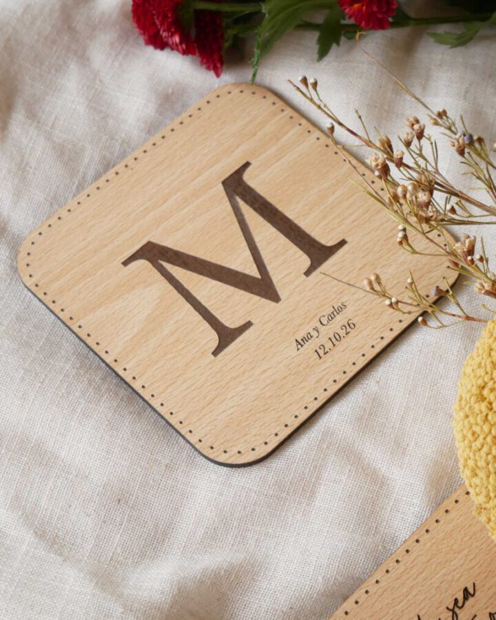 Posavasos artesanal de madera natural con inicial grabada a láser, nombres de los novios y fecha de boda en tipografía caligráfica