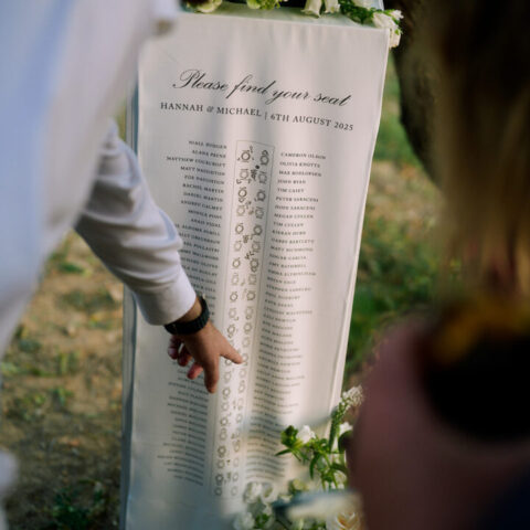 Seating plan de boda enrollado con tipografía caligráfica elegante y distribución de mesas pintado a mano sobre papel premium