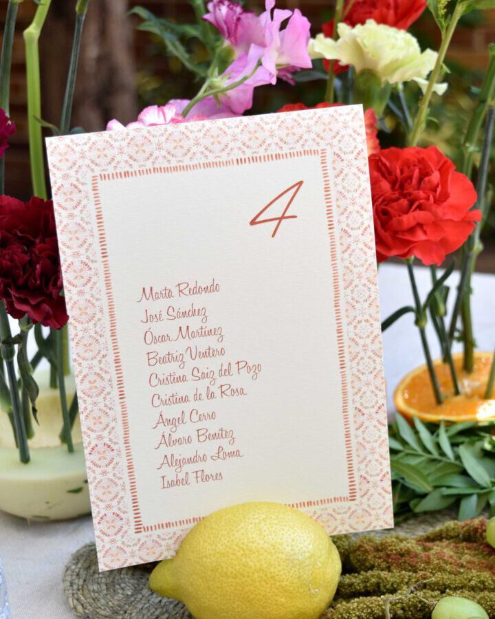 Tarjeta de seating plan modelo Azulejos con cenefa geométrica en tonos terracota presentada en ambiente mediterráneo con limones y flores
