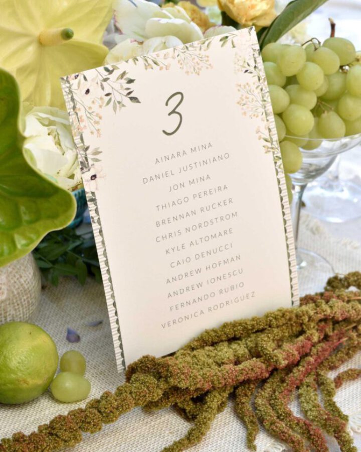 Tarjeta de seating plan de boda con número de mesa, listado de invitados y decoración botánica de hojas y flores pintadas en acuarela