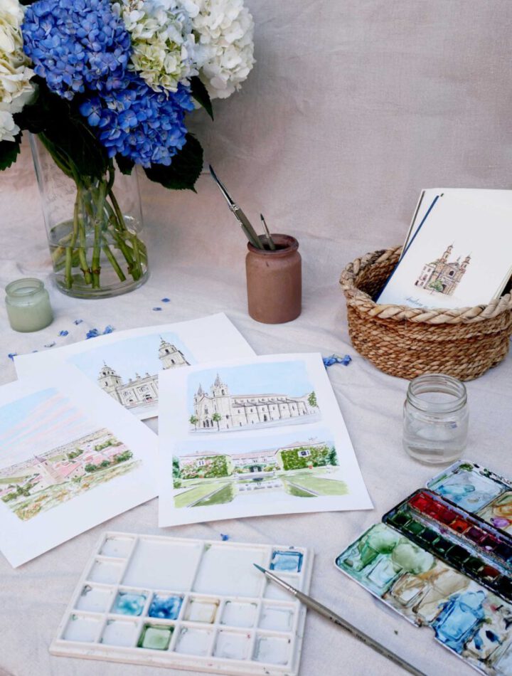 Mesa de trabajo de taller de acuarela con pinturas, pinceles, paleta de colores y obras terminadas de paisajes y arquitectura pintados a mano