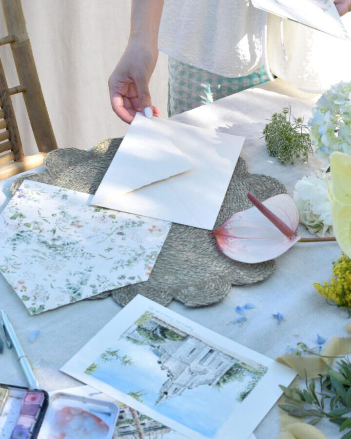 Mesa de trabajo del estudio con invitaciones de boda artesanales ilustradas en acuarela flores naturales y materiales de papelería