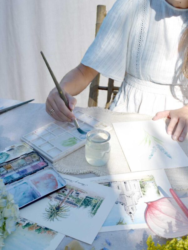 Ilustradora trabajando en su estudio creando invitaciones de boda artesanales con técnica de acuarela rodeada de materiales premium