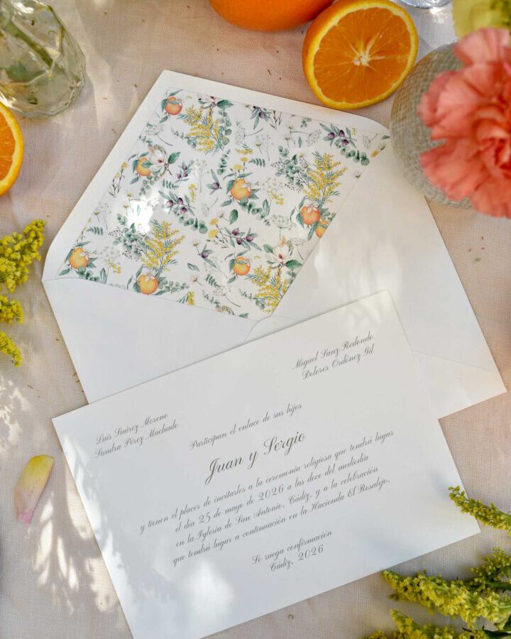 Composición lifestyle de la colección Azahar con invitación y sobre entre naranjas frescas, flores y follaje natural