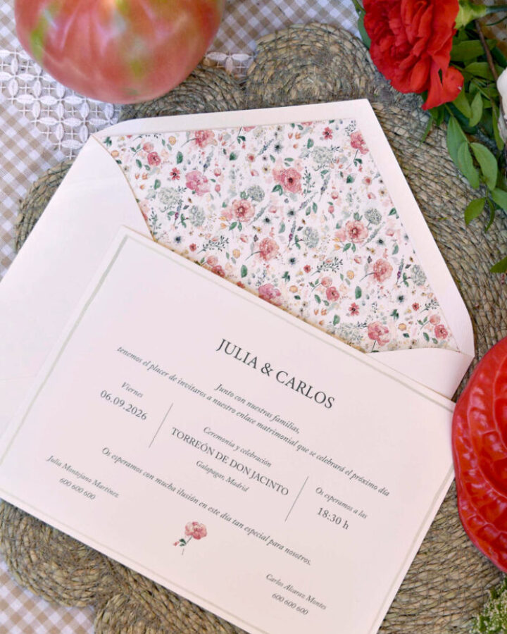 Invitación de boda artesanal con motivos florales en acuarela junto a sobre con forro estampado presentada en escena de estilismo natural