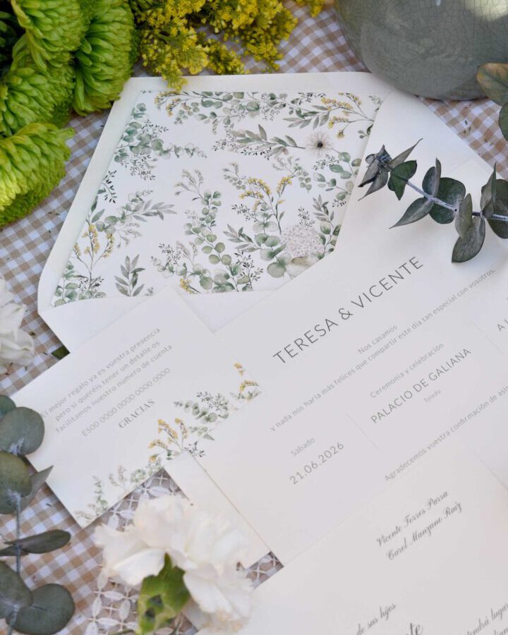 Invitaciones de boda coleccion Bosque con hojas verdes y ramas silvestres en composicion lifestyle sobre mantel de cuadros