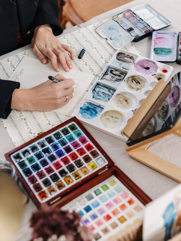 Artista de acuarela pintando en directo ilustraciones personalizadas durante una boda con paleta de colores y pinceles profesionales