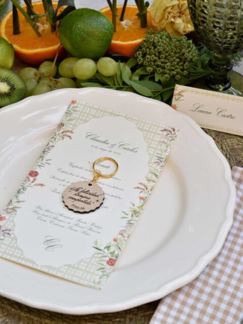 Llavero circular de madera grabado con texto personalizado junto a invitación de boda en acuarela como detalle para invitados