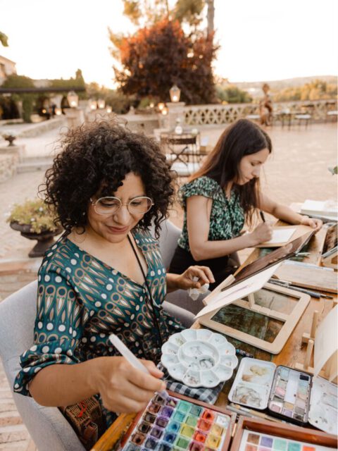 Dos artistas del equipo creativo pintando acuarelas a mano al aire libre con paletas de pigmentos y pinceles profesionales