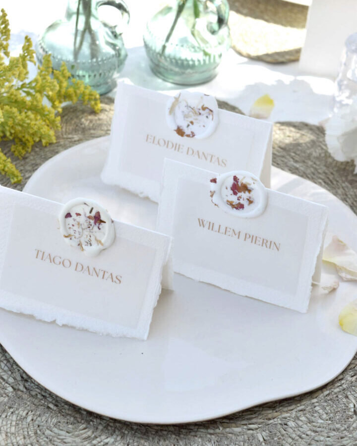 Marcasitios artesanos sobre papel blanco con nombres impresos en mayúsculas y sello decorativo de flores secas naturales