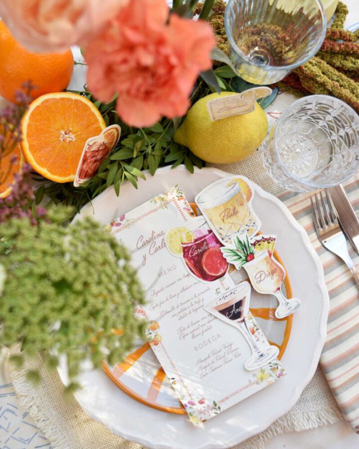 Conjunto de marcasitios con forma de copa de cóctel y minuta de boda con ilustraciones artesanales sobre plato decorado en mesa nupcial
