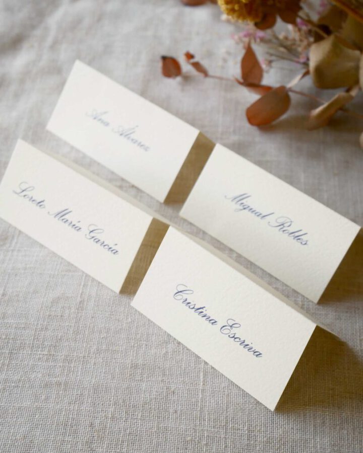 Marcasitios dípticos impresos con nombres de invitados en tipografía caligráfica sobre papel premium color natural