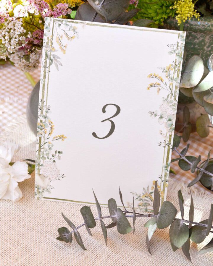 Mesero de boda Bosque con número de mesa enmarcado por orla de hojas y eucalipto pintadas a mano en acuarela sobre estilismo natural
