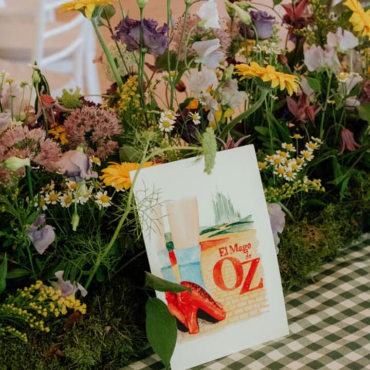 Mesero de boda ilustrado con portada de película pintada en acuarela sobre mantel de cuadros verdes entre arreglos florales