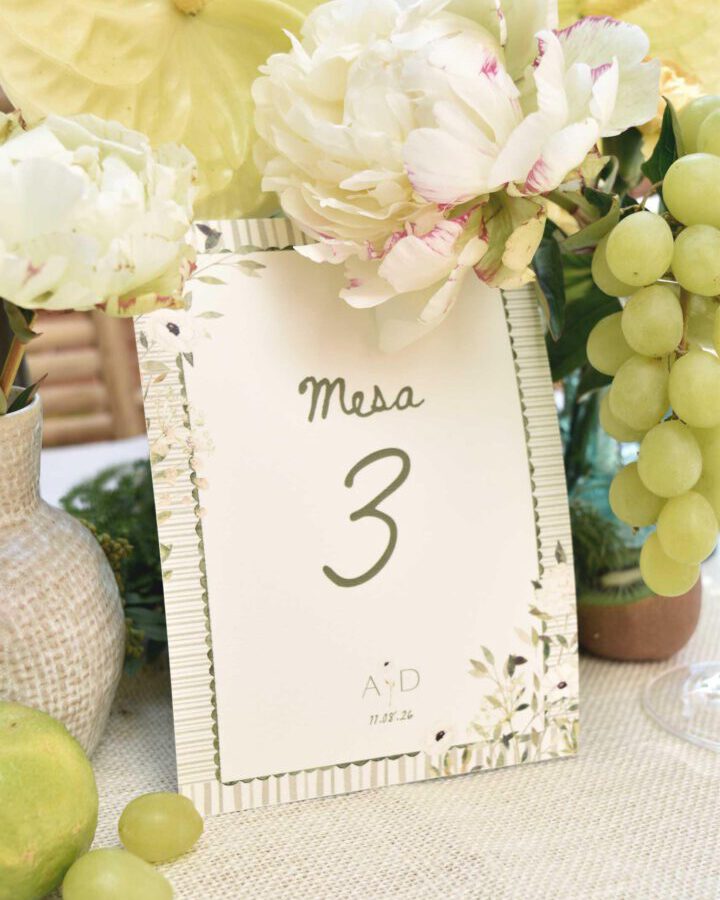 Mesero de boda con número de mesa en caligrafía, monograma de los novios y orla botánica pintada a mano con borde de pespunte decorativo