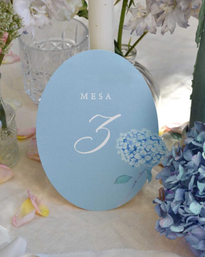 Mesero de boda con fondo celeste y número de mesa tres en tipografía caligráfica decorado con hortensias azules en acuarela artesanal
