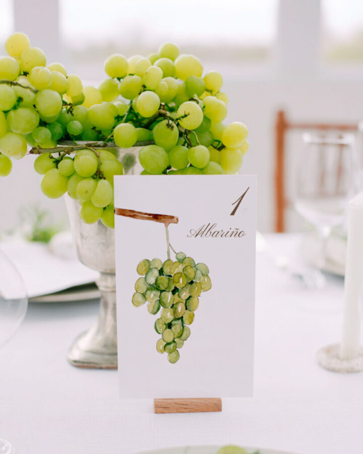 Mesero de mesa para boda coleccion Uvas con numero de mesa e ilustracion de racimo de uva Albarino pintado en acuarela artesanal presentado en ambientacion con uvas verdes frescas