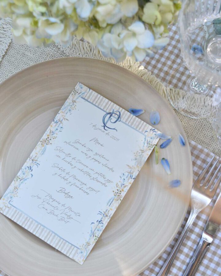 Minuta de boda Margarot con guirnalda de margaritas sobre plato blanco con hortensias azules y mantel de cuadros campestre