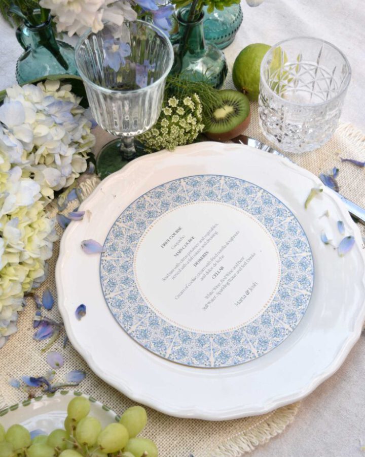 Minuta circular boda elaboradas artesanalmente orla azul geométrica mesa flores uvas kiwis cristalería vajilla elegante