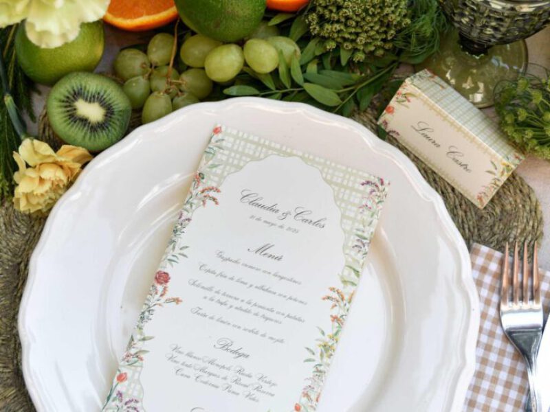 Minuta de boda personalizada sobre plato blanco con marco floral pintado a mano en acuarela y detalle de estampado tartán verde