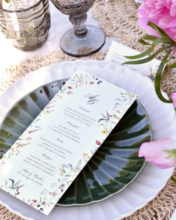 Minuta de boda colección Frida con orla floral multicolor sobre plato cerámico decorativo rodeada de peonías rosas y elementos bohemios