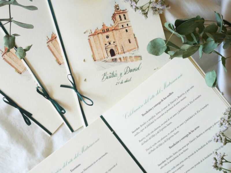 Conjunto de misales de boda con portada ilustrada en acuarela artesanal representando una iglesia y lazo verde oscuro decorativo