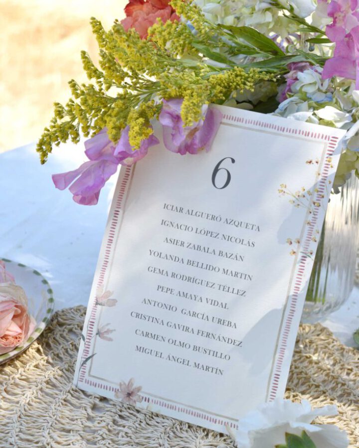 Tarjeta de seating plan modelo Brisa con marco decorativo floral y tipografía serif elegante sobre papel premium con lista de invitados