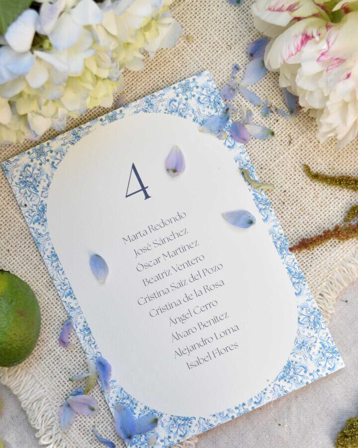 Seating de boda Mediterráneo de Trantan Estudio con marco ornamental azul sobre tela de lino con rosas y pétalos azules