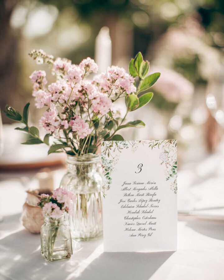 Seating plan de boda campestre con hojas pintadas en acuarela a mano ambientado sobre mesa nupcial con flores silvestres rosas