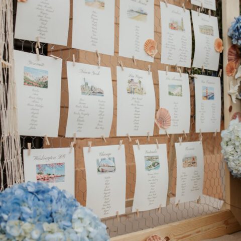 Seating plan de boda ilustrado con tarjetas individuales por mesa decoradas con acuarela artesanal y detalles marineros colgados en estructura decorativa