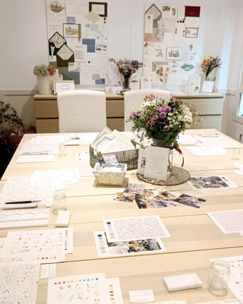 Mesa de trabajo preparada para taller de acuarela con materiales artísticos, muestras de papelería y pinceles en espacio luminoso y agradable